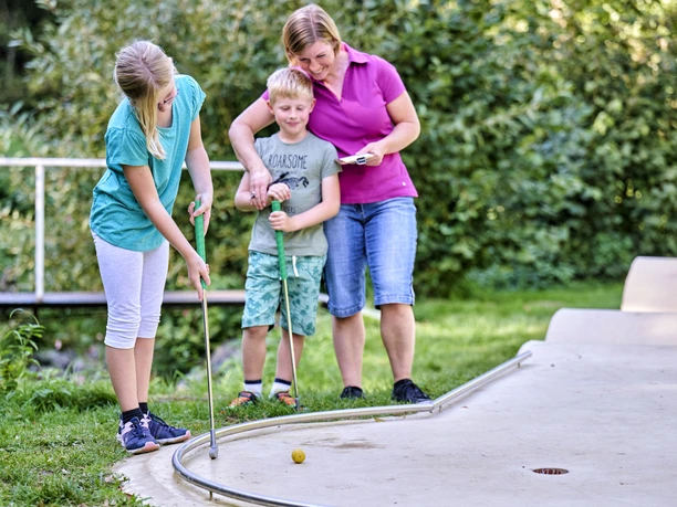 Bei Louis gibt es neben weiteren Angeboten auch eine Minigolfbahn Eine Mutter spielt mit zwei Kindern Minigolf