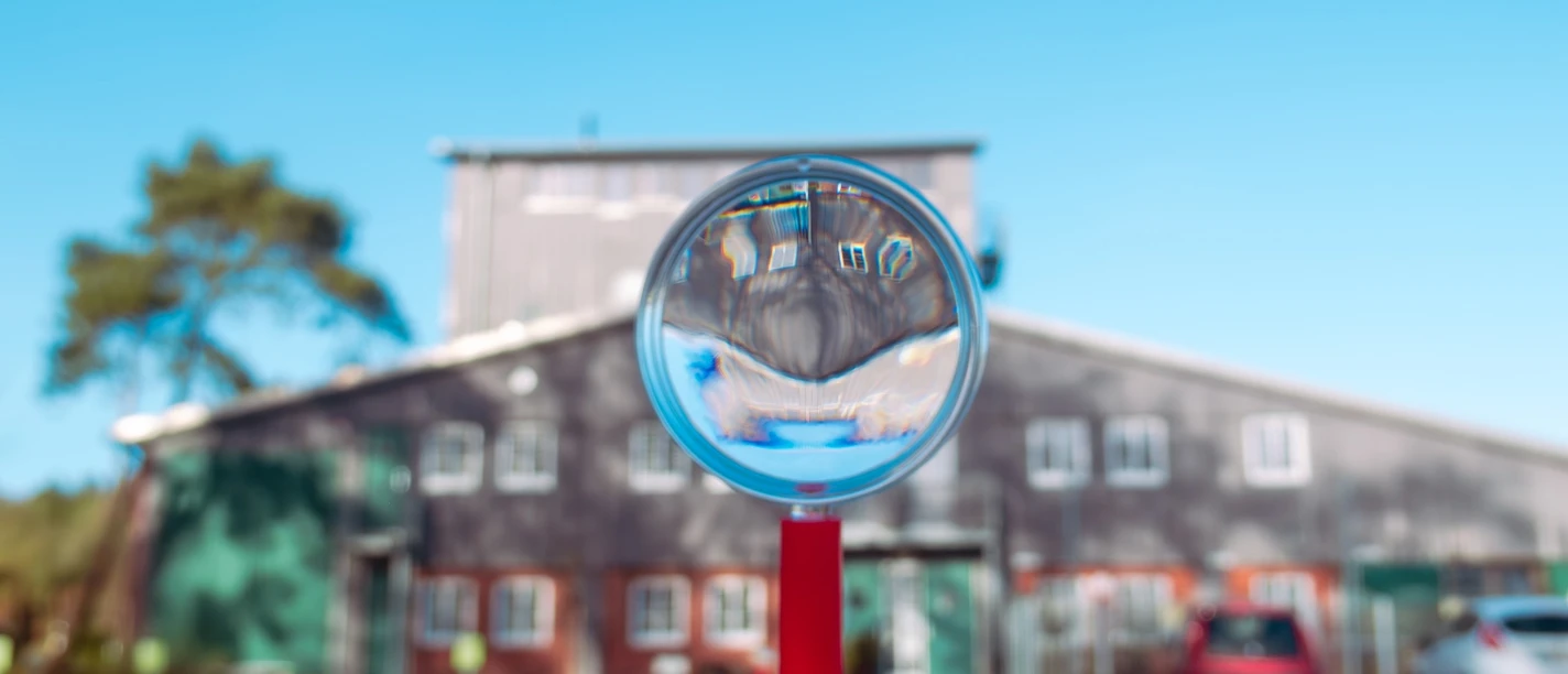 Ostersuche MoorIZ Ahlenmoor Lupe mit rotem Griff fokussiert den Blick auf das MoorInformationsZentrum, das sich unter klarem, blauem Himmel spiegelt.