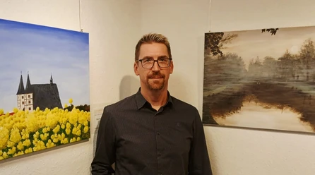 Andreas Rätsch Geithain Künstler Andreas Rätsch steht in einer Ausstellung vor seinen Bildern.