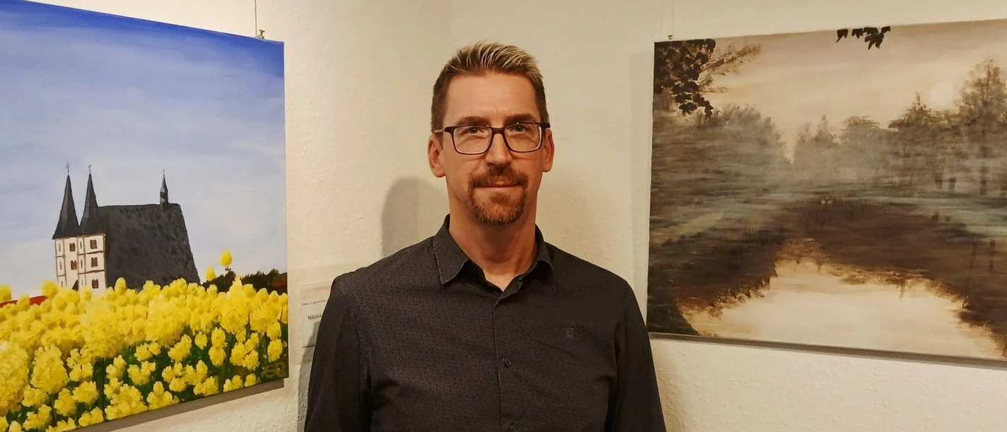 Andreas Rätsch Geithain Künstler Andreas Rätsch steht in einer Ausstellung vor seinen Bildern.