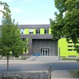 Ostfalia Hochschule_C-Gebaeude_HD_16zu9.jpg Modernes Hochschulgebäude mit grauer Fassade und leuchtend grünen Akzenten zwischen Bäumen.