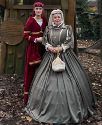 LAK: Mütter & Töchter Erzähltheater Zwei Frauen in historischen Kleidern posieren im Freien vor einer hölzernen Kulisse im Herbst.