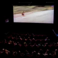Filmhaus, Kinosaal In einem abgedunkelte Kinosaal schaut ein Publikum einen Film auf großer Leinwand.
