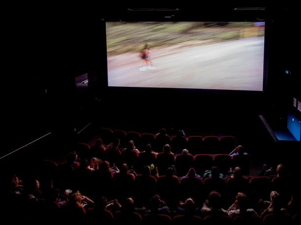 Filmhaus, movie theater In a darkened movie theater, an audience watches a film on a big screen.