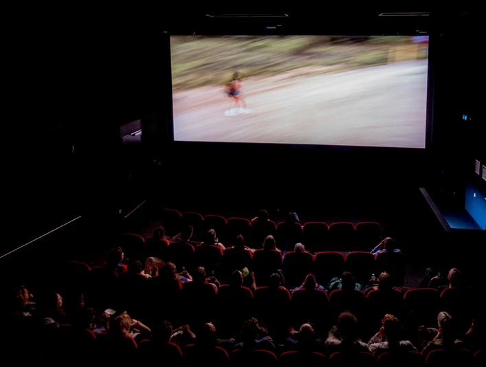 Filmhaus, movie theater In einem abgedunkelte Kinosaal schaut ein Publikum einen Film auf großer Leinwand. In a darkened movie theater, an audience watches a film on a big screen.