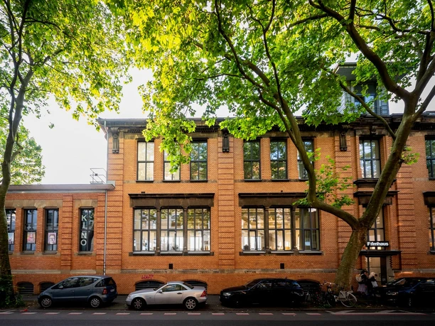 Filmhaus, Außenansicht Ein Backsteingebäude umgeben von Bäumen an einem sonnigen Tag.