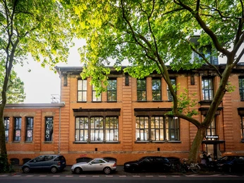 Filmhaus, exterior view Ein Backsteingebäude umgeben von Bäumen an einem sonnigen Tag.A brick building surrounded by trees on a sunny day.