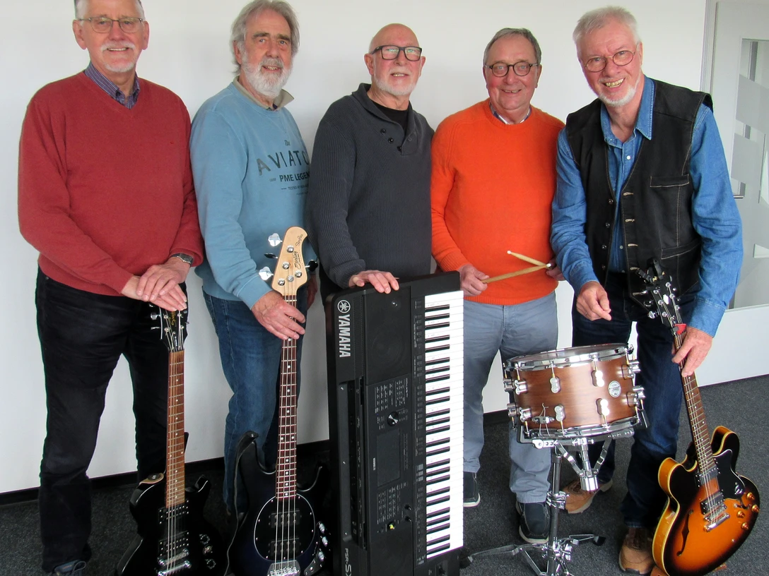 IMG_1160 (1).jpg Fünf Männer stehen nebeneinander, vier halten Musikinstrumente: zwei E-Gitarren, einen E-Bass, ein Keyboard und ein Schlagzeug mit Sticks.