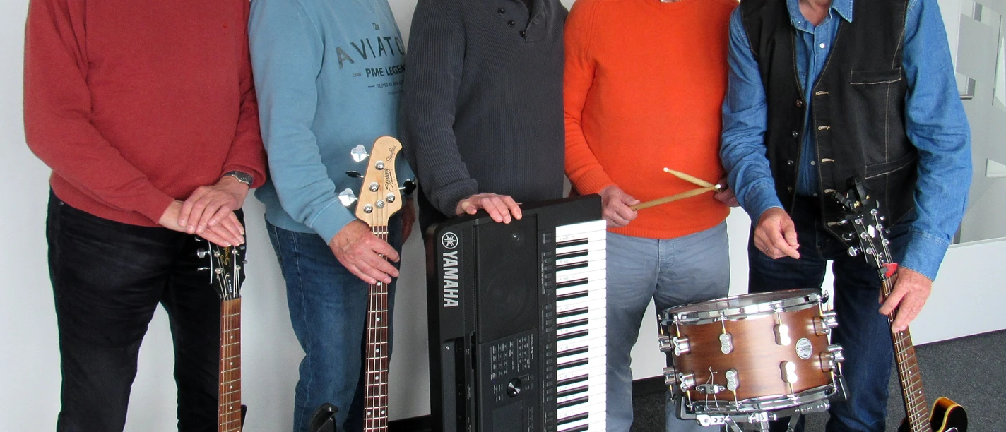 IMG_1160 (1).jpg Fünf Männer stehen nebeneinander, vier halten Musikinstrumente: zwei E-Gitarren, einen E-Bass, ein Keyboard und ein Schlagzeug mit Sticks.