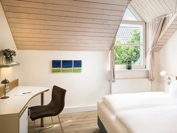 Doppelzimmer im Flussbett Hotel Helles Hotelzimmer mit Doppelbett, Schreibtisch, Holzdecke und Fenster unter Dachschräge.