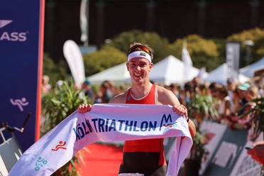 Köln Triathlon Triathlet im Zielbereich des Köln Triathlons mit breitem Banner in sonniger Kulisse