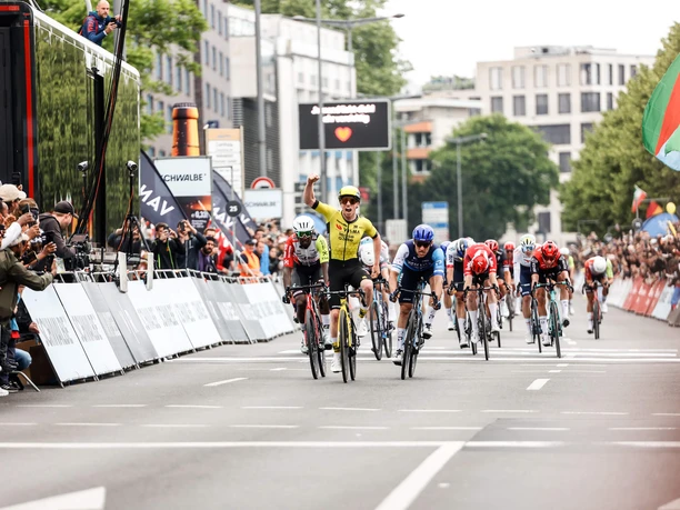 Rund um Köln Radsportler im Zielsprint vor jubelnder Menge in städtischer Kulisse.