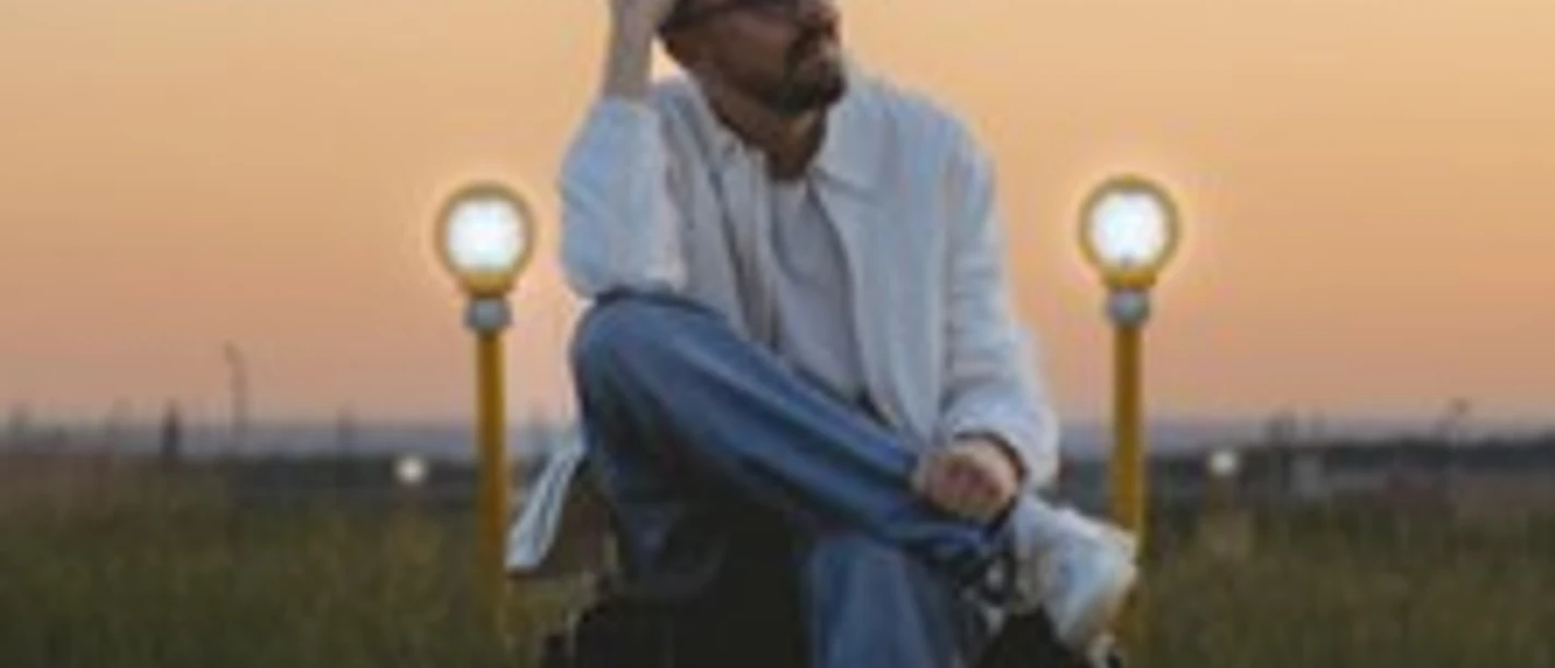 Eine Person sitzt im Gras bei Sonnenuntergang zwischen drei leuchtenden Lampen.