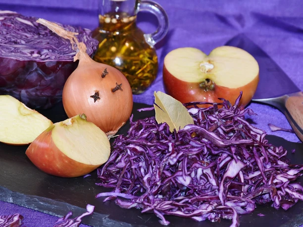 Hospizgruppe Kochen mit Trauernden Geschnittenes Rotkraut mit Apfelstücken, Zwiebel mit Nelken, Lorbeerblatt und Ölflasche auf dunkler Platte.