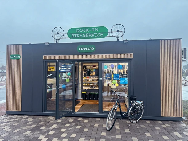 Dock-In Simple4Q.jpg Moderner Fahrradservice-Container mit offener Tür, bunten Schildern und geparktem Fahrrad davor.