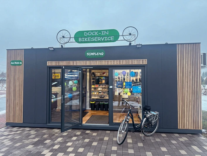 Dock-In Simple4Q.jpg Moderner Fahrradservice-Container mit offener Tür, bunten Schildern und geparktem Fahrrad davor.