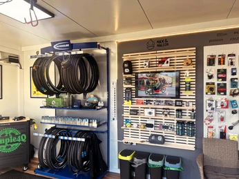 Dock-In Werkstatt.jpg Innenraum einer modernen Fahrradwerkstatt mit aufgeräumten Regalen voller Zubehör und Ersatzteilen.