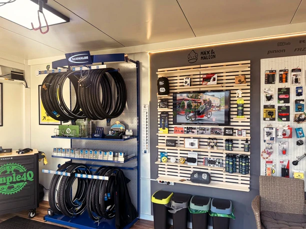 Dock-In Werkstatt.jpg Innenraum einer modernen Fahrradwerkstatt mit aufgeräumten Regalen voller Zubehör und Ersatzteilen.