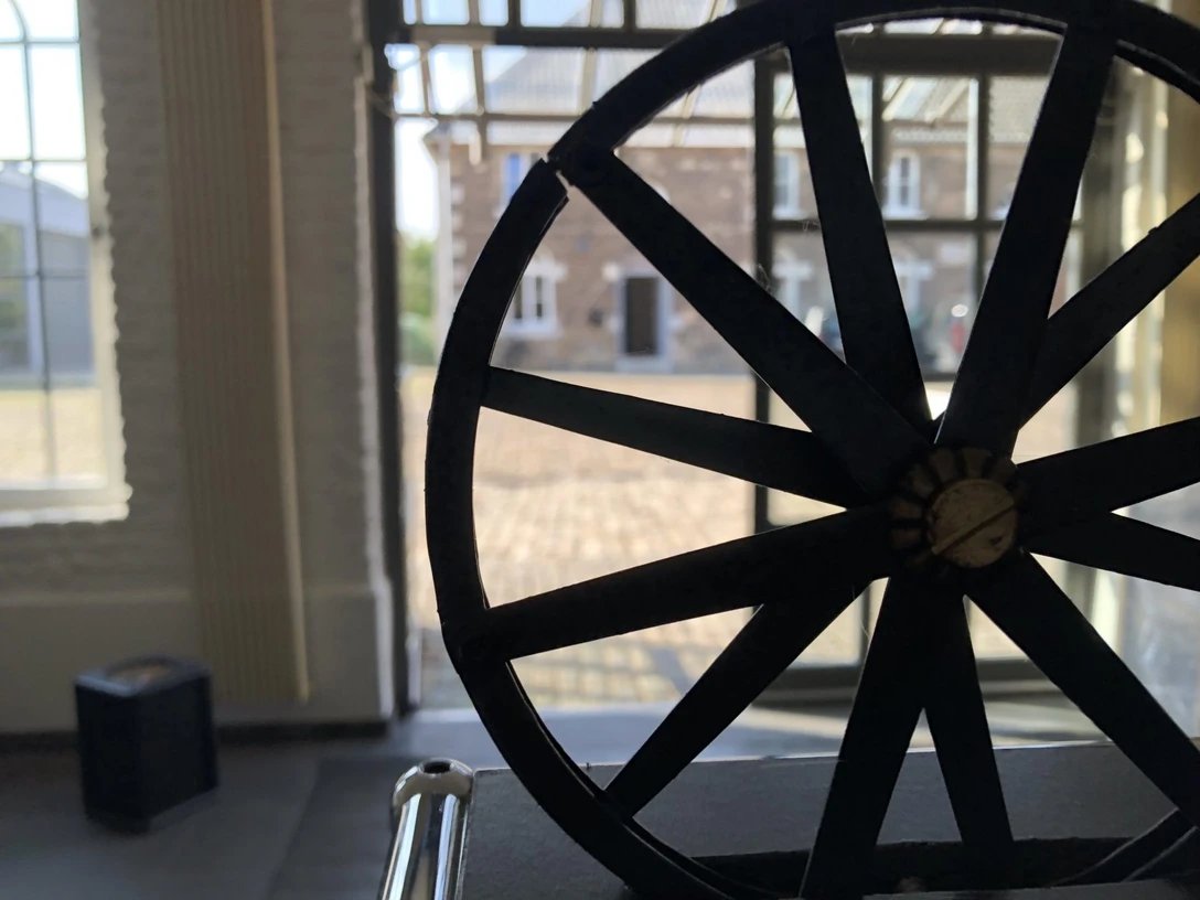 Im Vordergrund ist ein altes Rad ausgestellt. Dahinter erkennt man den Eingang des Museums und einen gepflasterten Vorplatz.