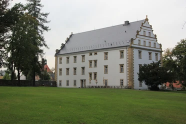 Schluckenauer Schloss Böhmische Schweiz Weißes Schloss mit Ziergiebel, umgeben von einer Rasenfläche und Bäumen.