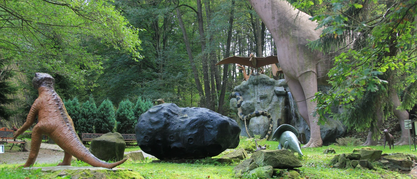 Dinosauriermodelle im Wald, darunter ein großer aufgerichteter und ein kleinerer Dinosaurier.