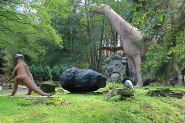 Urzeitpark Sebnitz Dinosauriermodelle im Wald, darunter ein großer aufgerichteter und ein kleinerer Dinosaurier.
