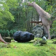 Urzeitpark Sebnitz Dinosauriermodelle im Wald, darunter ein großer aufgerichteter und ein kleinerer Dinosaurier.