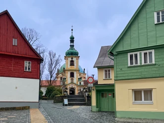 Bunte Häuser und Kirche mit Zwiebelturm in einer gepflasterten Straße.