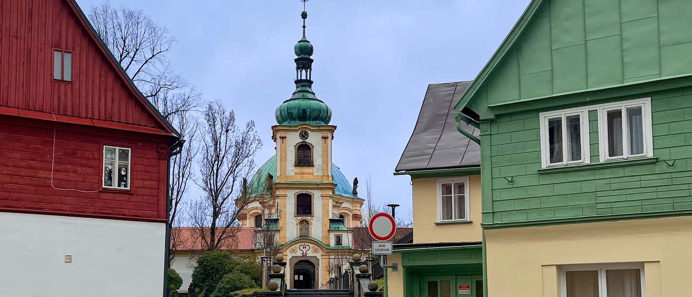 Ceská Kamenice mit Wallfahrtskirche Bunte Häuser und Kirche mit Zwiebelturm in einer gepflasterten Straße.
