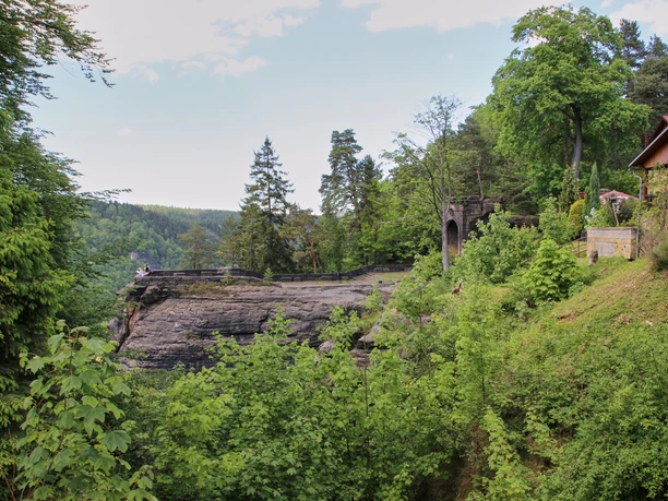 Belvedere Hrensko Aussichtsplattform Waldlandschaft mit Holzhaus und Felsvorsprung, im Hintergrund eine Aussichtspattform.