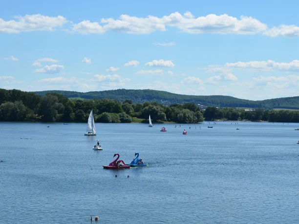 Segel- und Tretboote auf dem Salzgittersee mit grünem Höhenzug und blauem Himmel im Hintergrund