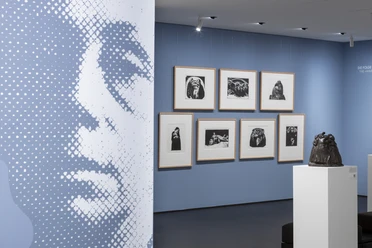 Käthe Kollwitz Museum Exhibition space with large-format portrait, framed graphics on blue wall and sculpture.