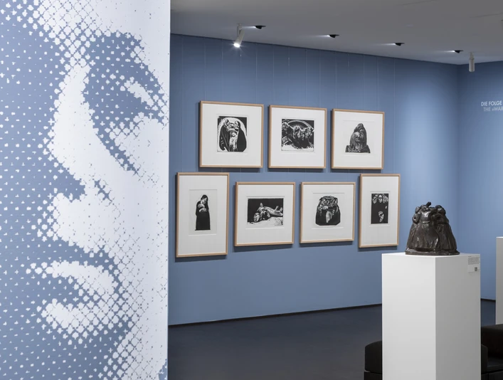 Käthe Kollwitz Museum Exhibition space with large-format portrait, framed graphics on blue wall and sculpture.