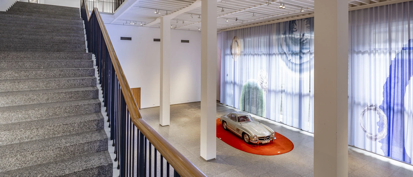 Museum für Angewandte Kunst Köln Heller Museumsraum mit breiter Treppe und silbernem Oldtimer auf rotem Podest im Erdgeschoss.
