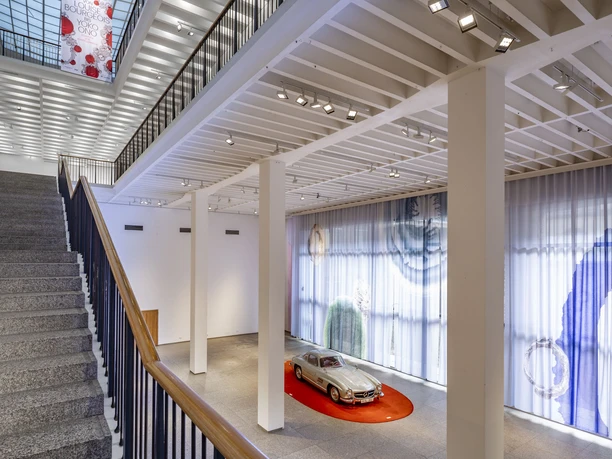 Museum of Applied Arts Cologne Bright museum room with wide staircase and silver vintage car on a red platform on the first floor.