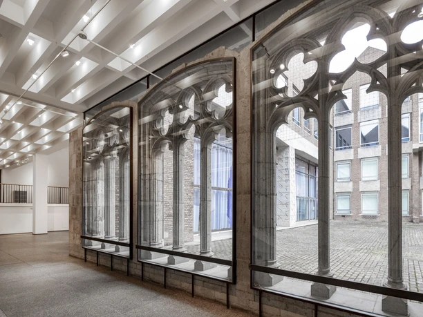 Museum für Angewandte Kunst Köln Großer Innenraum mit beleuchtetem Deckenraster und gotischen Steinbogenfenstern zum Innenhof.