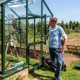 Foto Hoklartherm.jpg Ein Mann baut bei Sonnenschein ein grünes Glashaus im Garten auf und prüft die Tür.