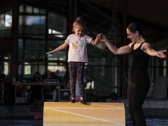 Erste Schritte beim Balancieren Eine Trainerin hält die Hand eines Mädchens und gibt Hilfestellung auf einer Rolle im Mitmachzirkus Aletsch Arena.A trainer holds a girl's hand and gives assistance on a roll in the Aletsch Arena hands-on circus.Une entraîneuse tient la main d'une fille et l'aide sur une roulade au cirque participatif Aletsch Arena.