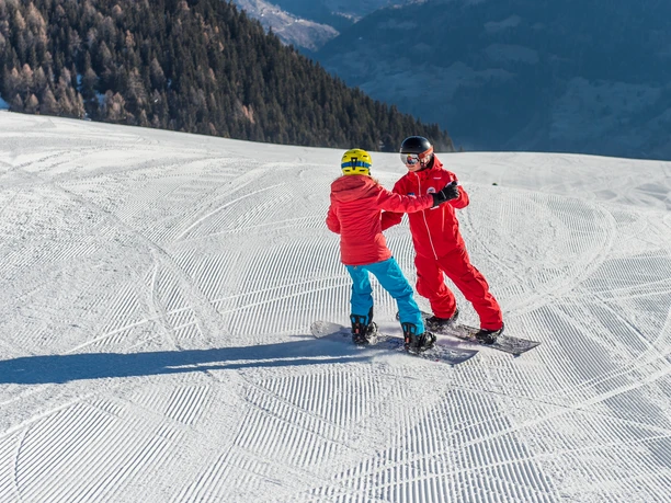 First balance exercises A child holds on to the instructor's hands and practises balance on the snowboard taster course in Riederalp.