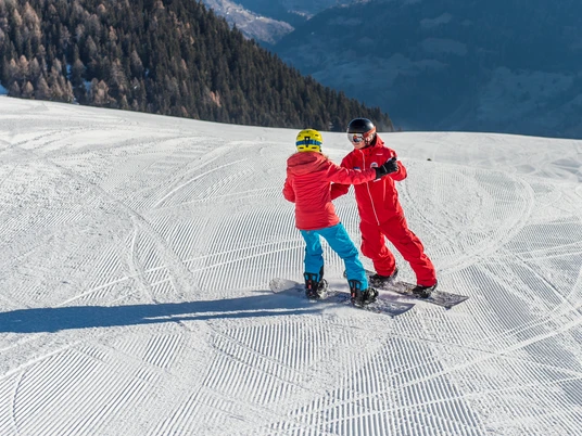 Premiers exercices d'équilibre Ein Kind hält sich an den Händen des Lehrers fest und übt im Snowboard Schnupperkurs Riederalp das Gleichgewicht.A child holds on to the instructor's hands and practises balance on the snowboard taster course in Riederalp.Un enfant s'accroche aux mains du moniteur et s'exerce à l'équilibre lors du cours d'essai de snowboard à Riederalp.