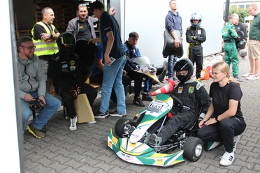 Jugendlicher im Kart vor dem Start, Trainerin gibt letzte Hinweise, weitere Teilnehmende warten.