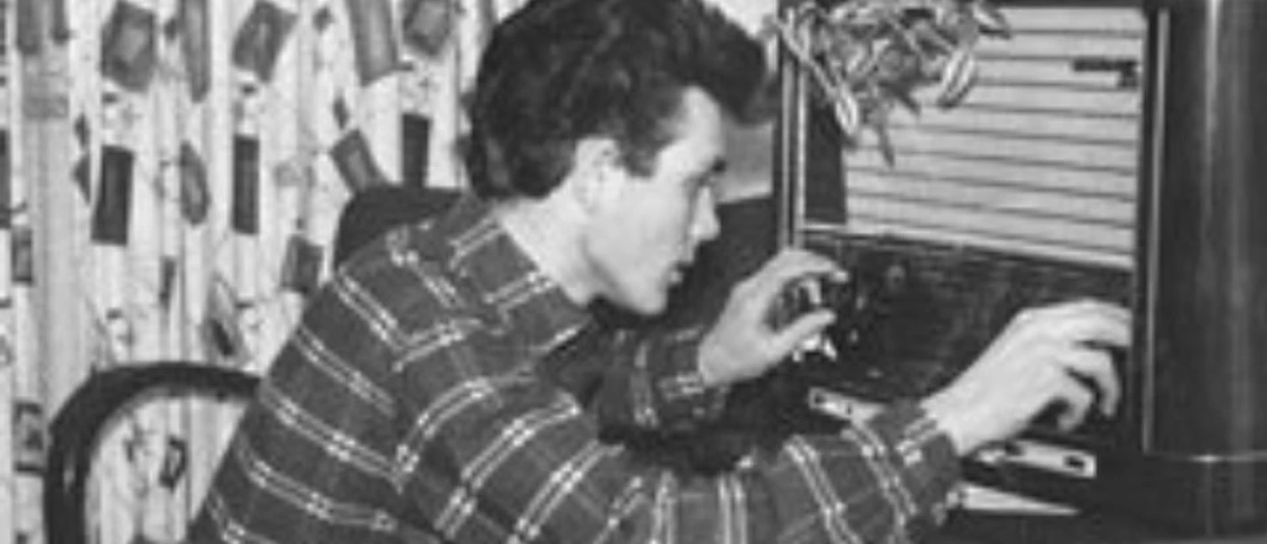 Das Lied vom Wirtschaftswunder Schwarzweißfoto eines jungen Mannes, der hockend an einem Röhrenradio die Einstellungen dreht.