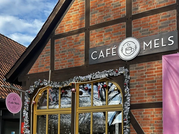 Außenansicht (Winter) (2) Fachwerkfassade des Café Mels mit winterlicher Dekoration und gelben Fenstern unter blauem Himmel.