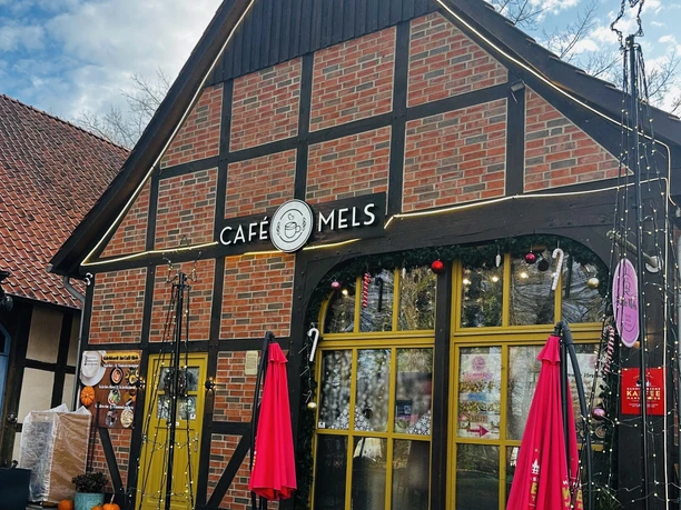 Außenansicht (Winter) (1) Backsteingebäude mit gelben Fenstern, roten Sonnenschirmen und winterlicher Dekoration vor dem Eingang