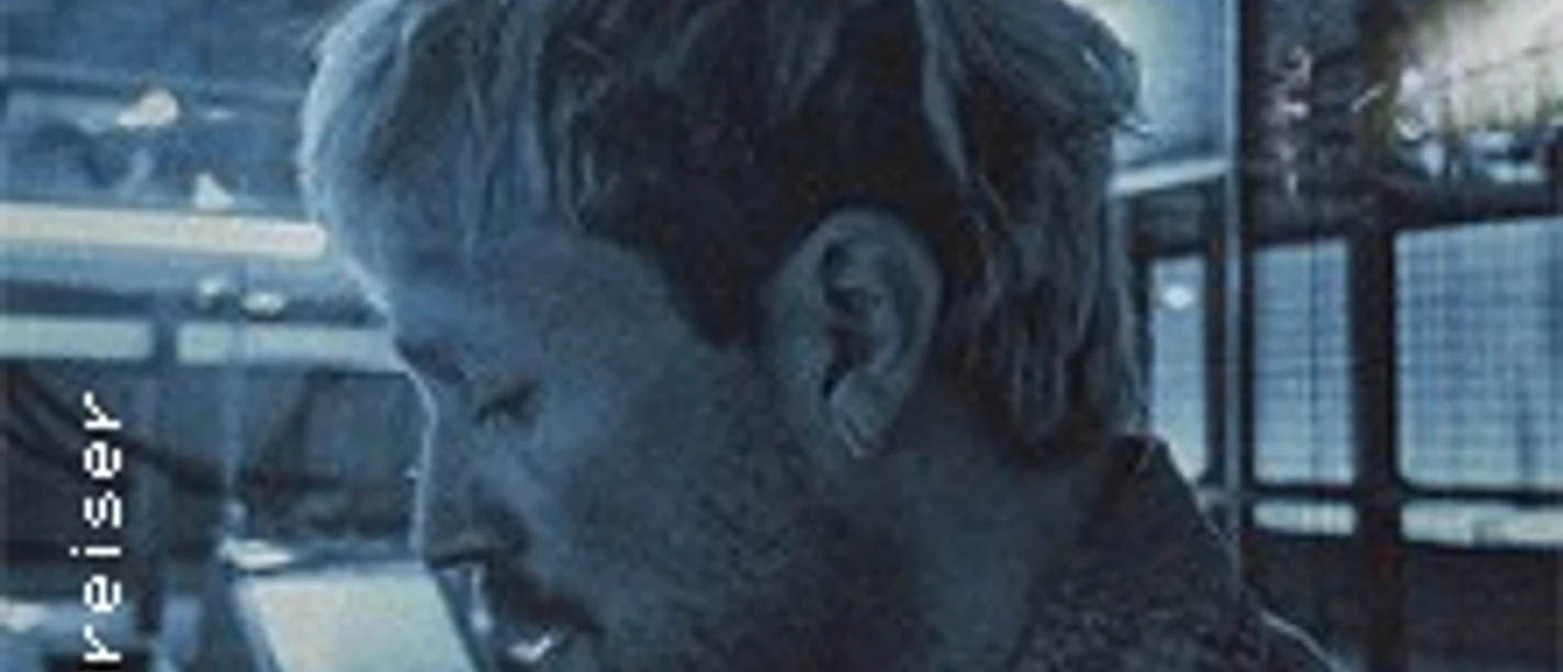 Eine Person mit hellem Haar steht in blauem Licht vor modernen Glasflächen.