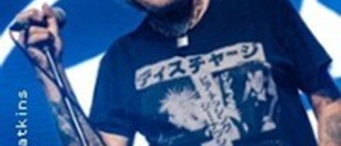 Älterer Musiker mit Mikrofon und Sonnenbrille auf einer Bühne vor blauem Hintergrund