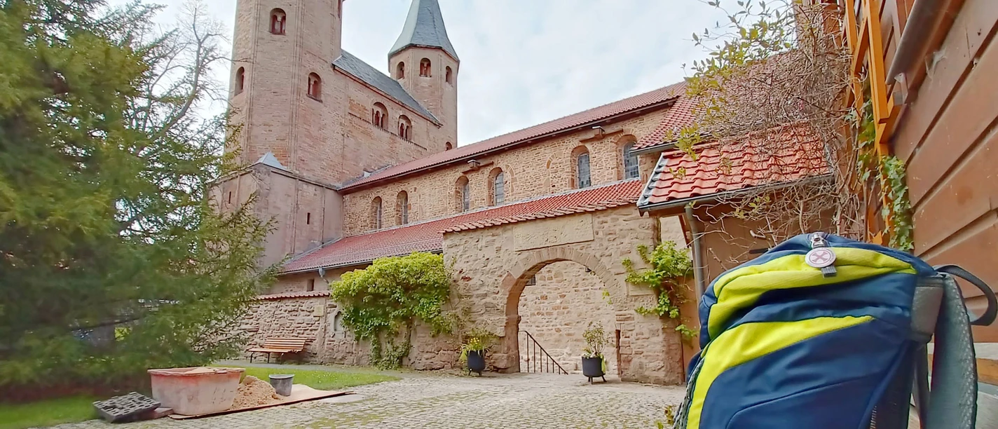 Backpack in front of the Drübeck monastery church, with stone walls and church steeples.