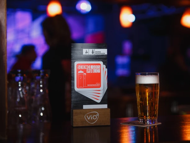 _MG_1243 ohne Datum (c) Sebastian Kühl.jpg Ein Glas Bier steht neben einem Flyer der Veranstaltungsreihe Science goes Public in einer Bar.
