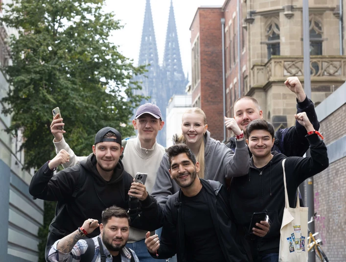 Pokémon GO Community Eine Gruppe posiert glücklich mit erhobener Faust. Im Hintergrund ragt der Kölner Dom hervor. A group poses happily with a raised fist. Cologne Cathedral looms in the background.