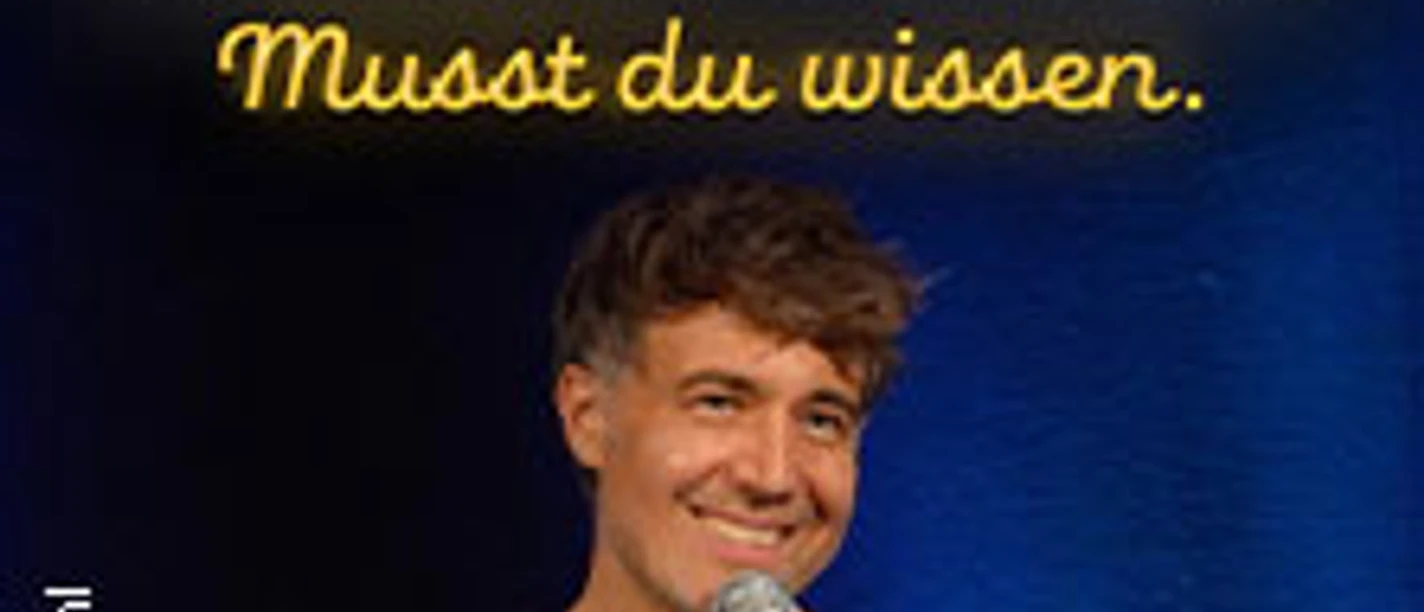 Ein Mann mit Mikrofon auf einer Bühnenkulisse, darüber ein heller Schriftzug vor blauem Hintergrund.